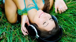 Smiling Girl Listens to Music on the Green Grass